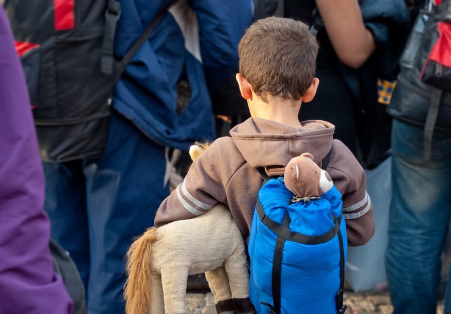 A child refugee holding a stuffed animal in a crowd